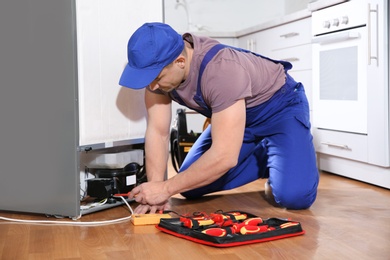 Photo of Male technician in uniform repairing refrigerator indoors