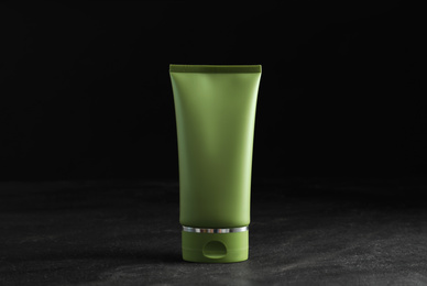 Photo of Tube of cosmetic product on grey stone table against black background