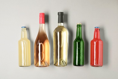Bottles with different alcoholic drinks on light background, top view