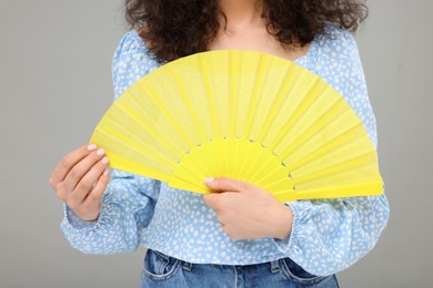 Photo of Woman holding hand fan on light grey background, closeup