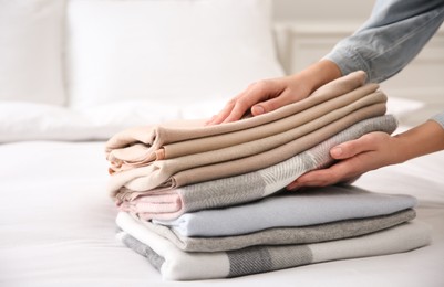 Woman with folded cashmere clothes on bed, closeup