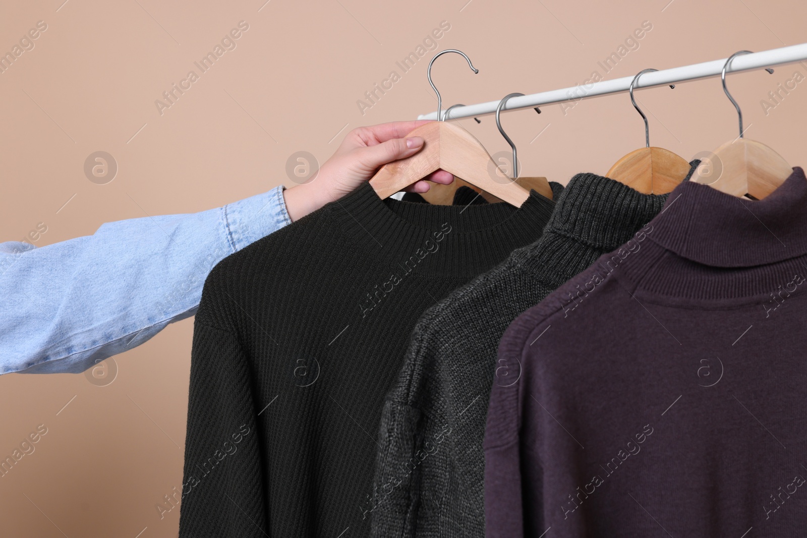 Photo of Woman taking sweater from rack on beige background, closeup