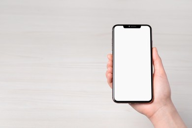 Photo of Woman holding smartphone with blank screen at white wooden table, top view. Mockup for design