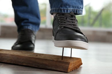 Photo of Careless man stepping on nails in wooden plank, closeup
