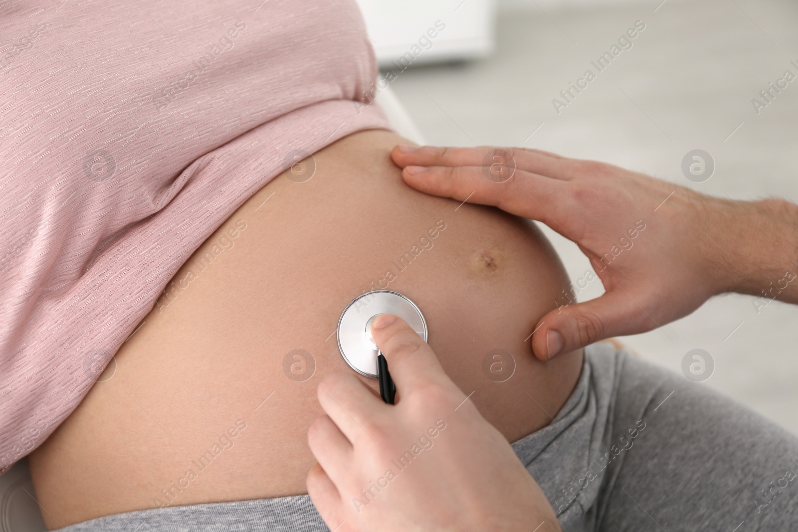 Photo of Doctor examining pregnant woman with stethoscope in clinic, closeup