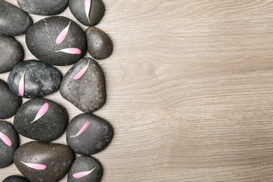 Photo of Spa stones with flower petals on wooden background, flat lay. Space for text