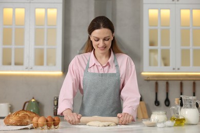 Photo of Making bread. Woman rolling raw dough at white table in kitchen