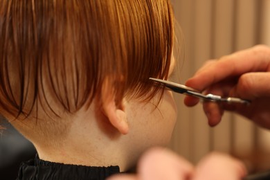 Professional hairdresser cutting boy's hair in beauty salon, closeup