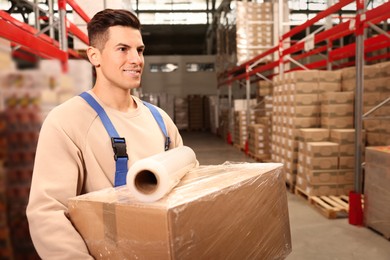 Photo of Worker with roll of stretch film and wrapped box in warehouse