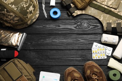 Photo of Frame of military first aid kit and uniform on wooden table, flat lay. Space for text