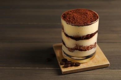 Photo of Delicious tiramisu in glass and coffee beans on wooden table, closeup. Space for text