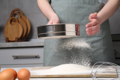 Woman sieving flour at table in kitchen, closeup