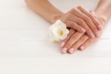 Photo of Closeup view of woman with flower at white wooden table, space for text. Spa treatment