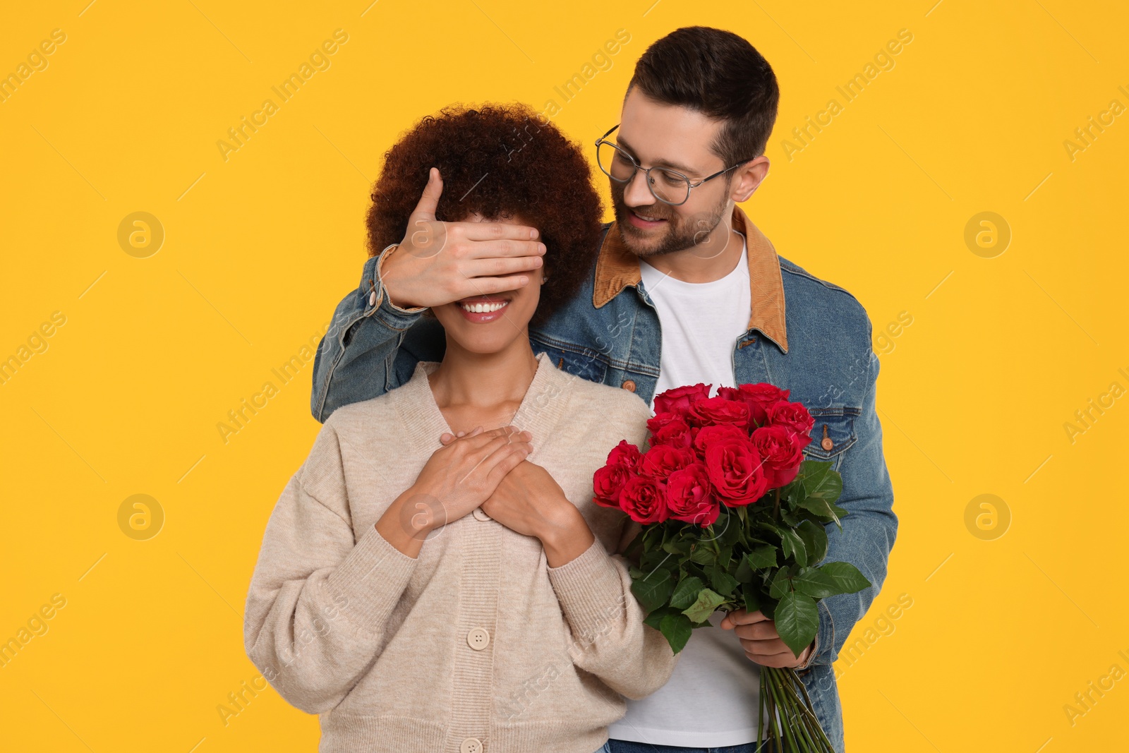 Photo of International dating. Handsome man presenting roses to his beloved woman on orange background