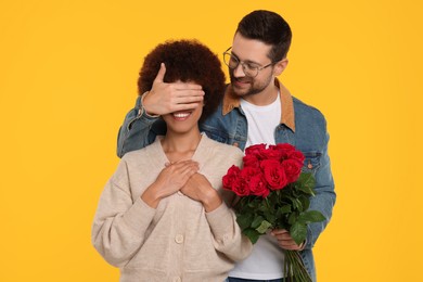 International dating. Handsome man presenting roses to his beloved woman on orange background