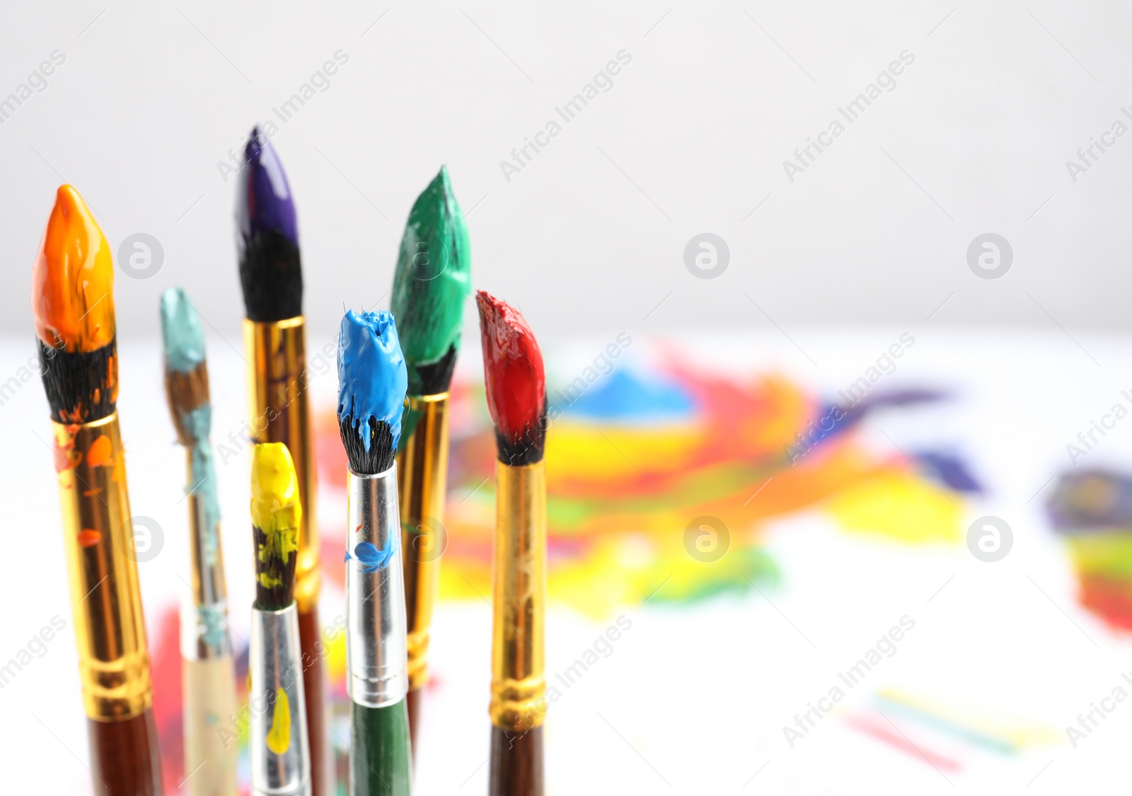 Photo of Brushes with colorful paints on blurred background, space for text