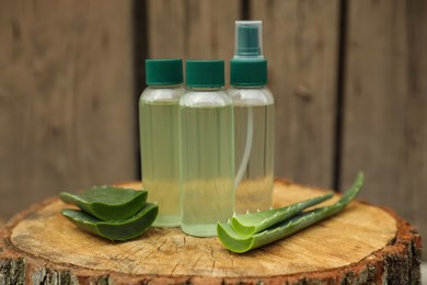 Photo of Bottlescosmetic products and sliced aloe vera leaves on wooden stump