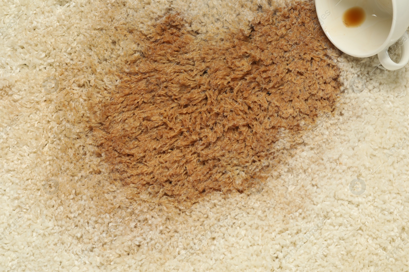 Photo of Overturned cup and spilled coffee on beige carpet, top view