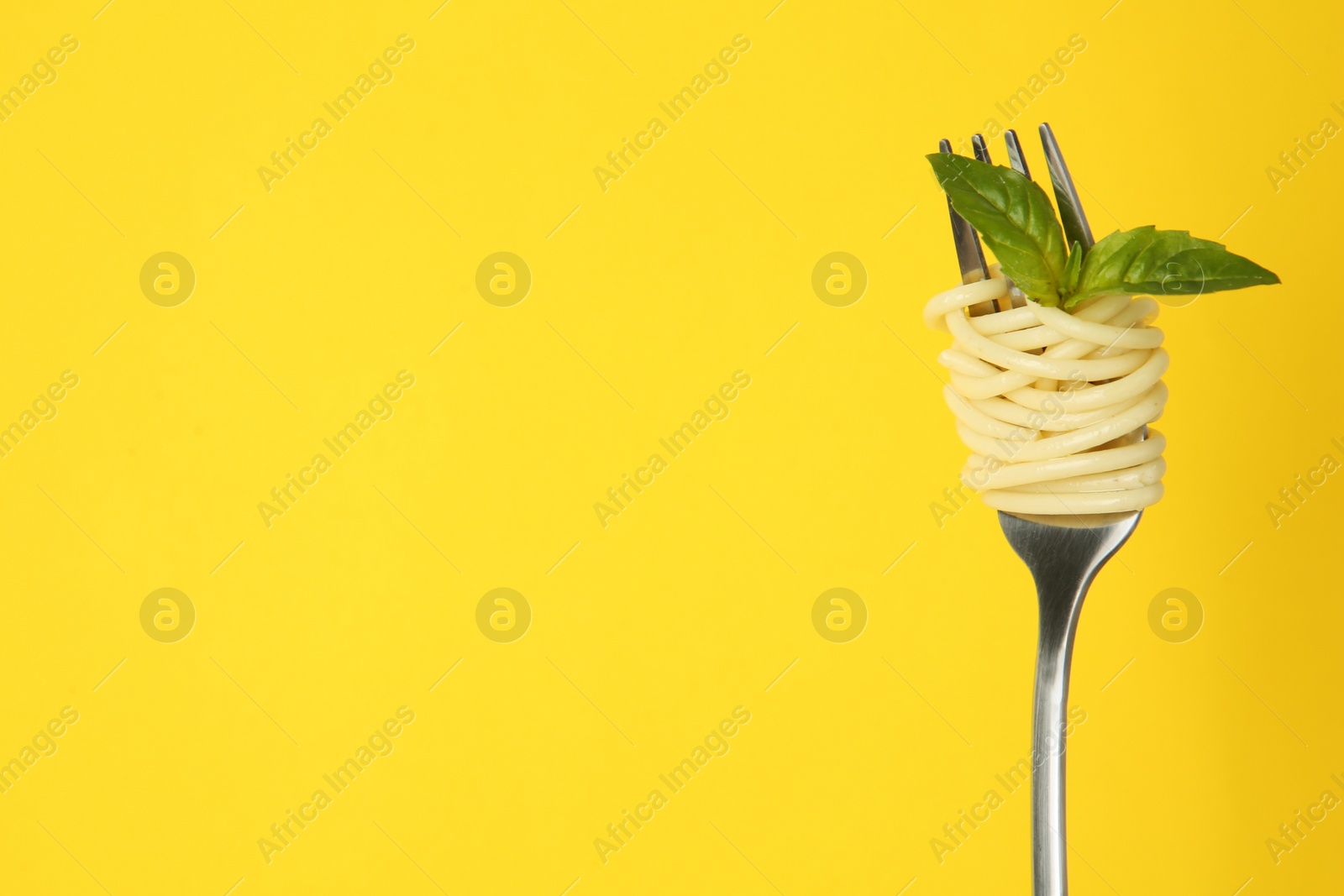 Photo of Fork with tasty pasta and basil leaves on yellow background, space for text