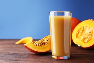 Tasty pumpkin juice in glass and cut pumpkin on wooden table against blue background. Space for text