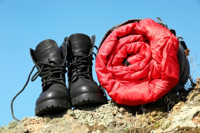 Photo of Boots and sleeping bag on rock outdoors. Camping equipment