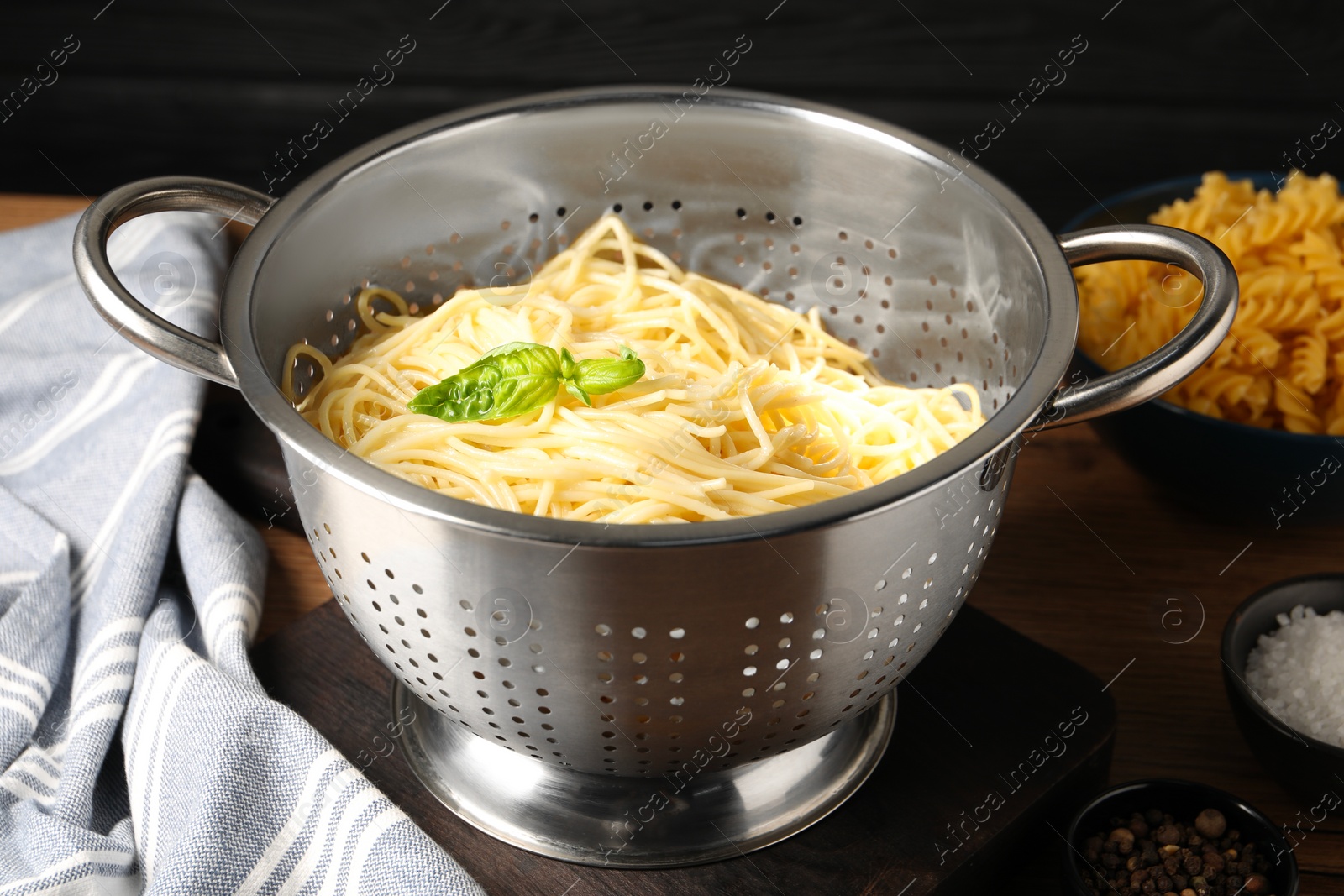 Photo of Cooked pasta in metal colander and spices on table, closeup