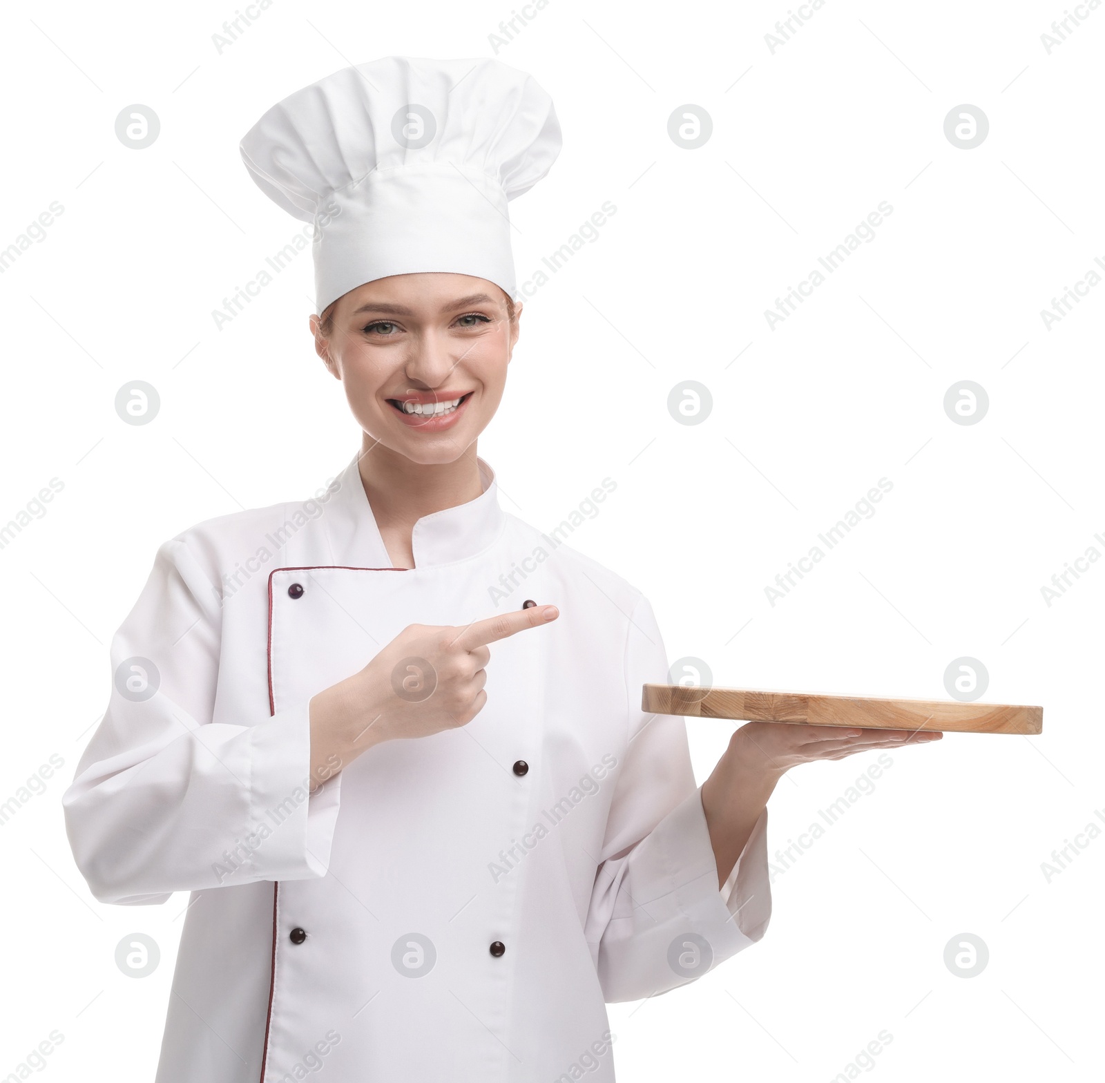 Photo of Happy woman chef in uniform pointing at empty wooden board on white background