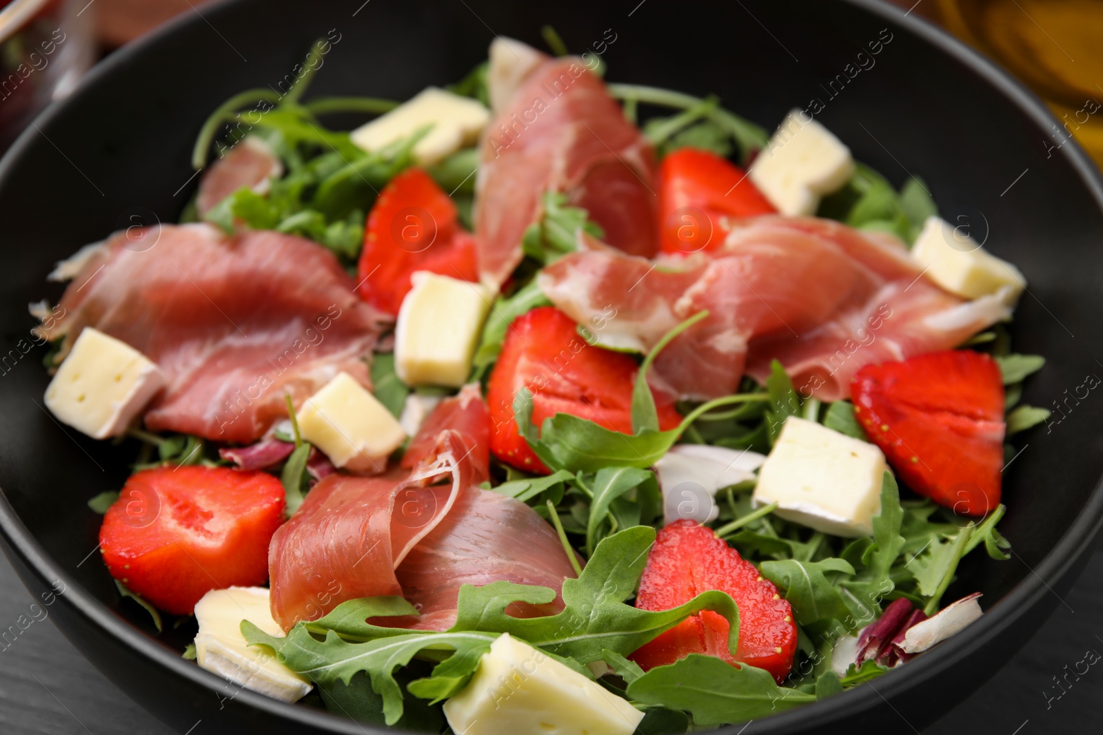 Photo of Tasty salad with brie cheese, prosciutto and strawberries in bowl, closeup