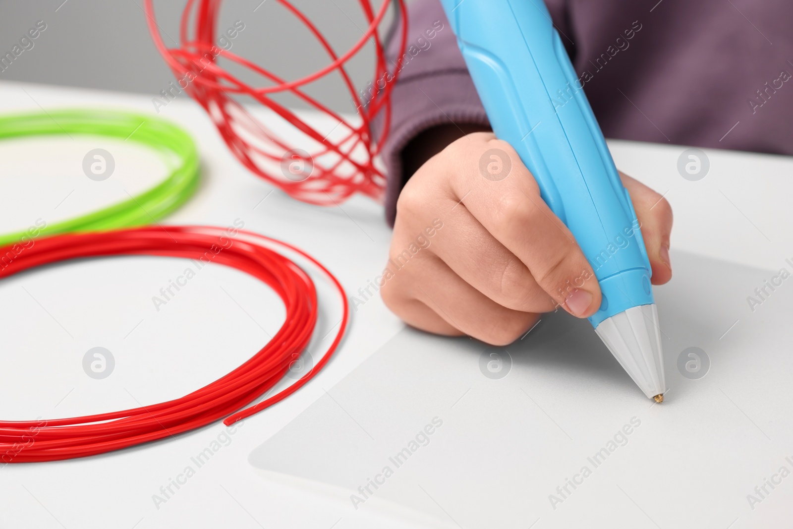 Photo of Boy drawing with stylish 3D pen at white table, closeup