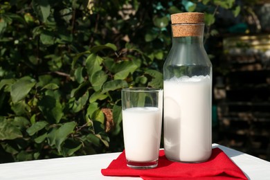 Glass and bottle of fresh milk on white wooden table outdoors. Space for text