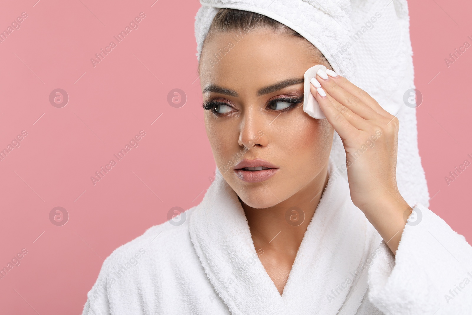 Photo of Beautiful woman removing makeup with cotton pad on pink background, space for text