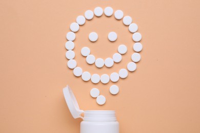 Photo of Happy face made of antidepressant pills and bottle on pale orange background, flat lay