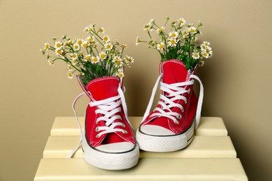 Photo of Beautiful tender chamomile flowers in red gumshoes on wooden table