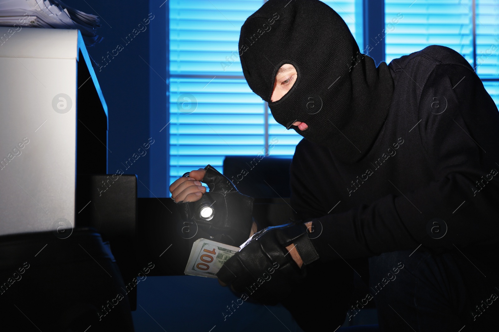 Photo of Thief taking money out of steel safe indoors at night