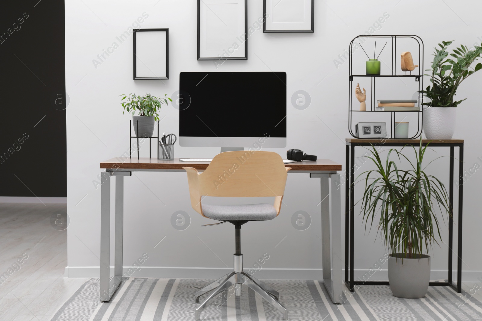 Photo of Cozy workspace with computer on desk, chair and houseplants near white wall at home