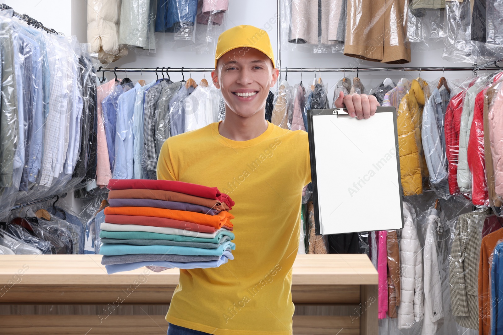 Image of Happy courier holding folded clothes and clipboard in dry-cleaning