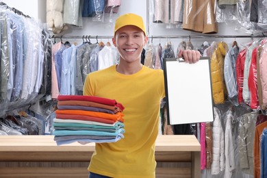 Image of Happy courier holding folded clothes and clipboard in dry-cleaning