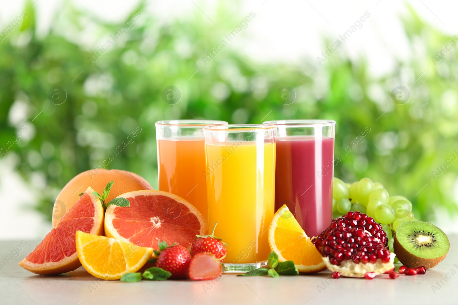 Photo of Three glasses with different juices and fresh fruits on table against blurred background