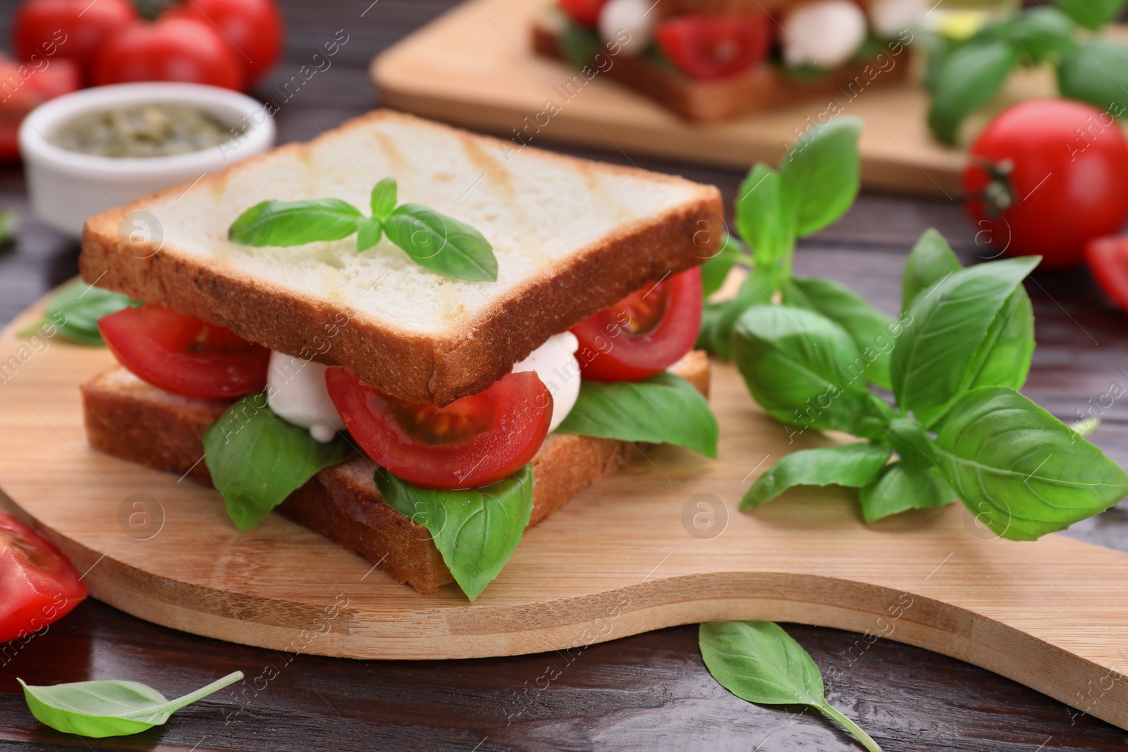 Photo of Delicious Caprese sandwich with mozzarella, tomatoes, basil and pesto sauce on wooden table, closeup