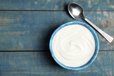 Bowl with creamy yogurt and spoon on blue wooden background, top view. Space for text