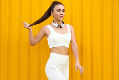 Photo of Young woman in sportswear with headphones near corrugated yellow metal wall