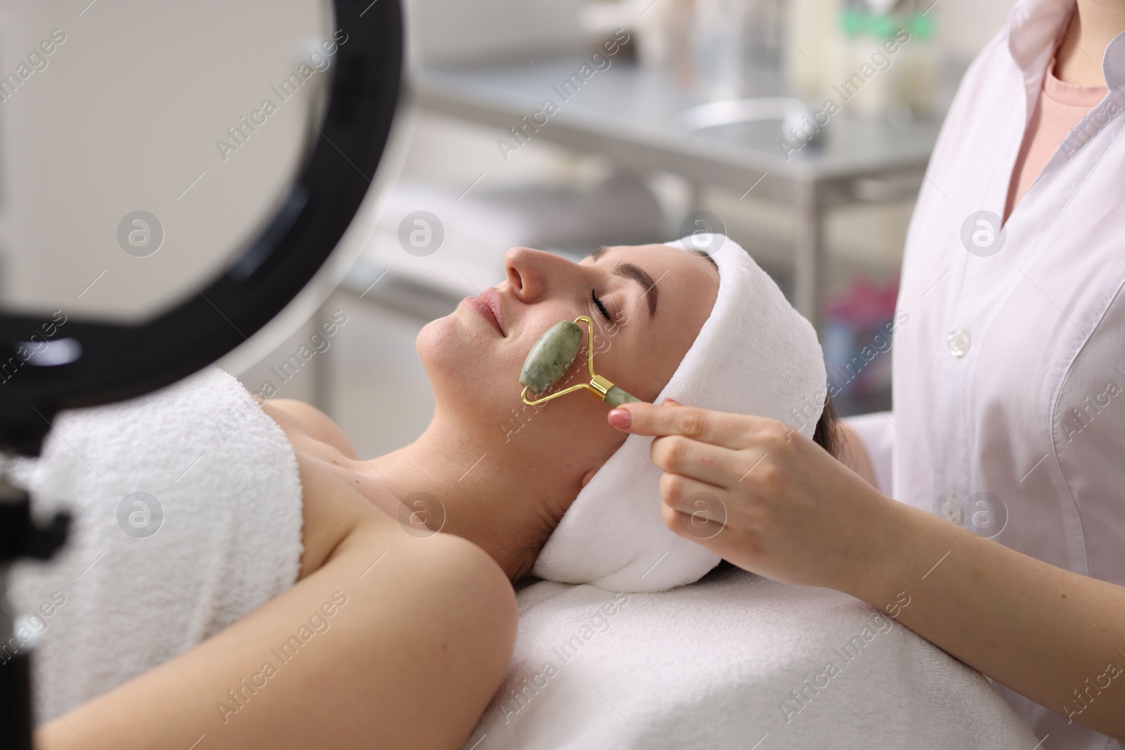 Photo of Cosmetologist making face massage with roller to client in clinic, closeup