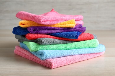 Photo of Stack of colorful microfiber cloths on light wooden table, closeup