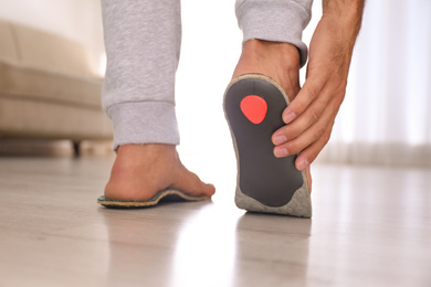 Photo of Man fitting orthopedic insole at home, closeup