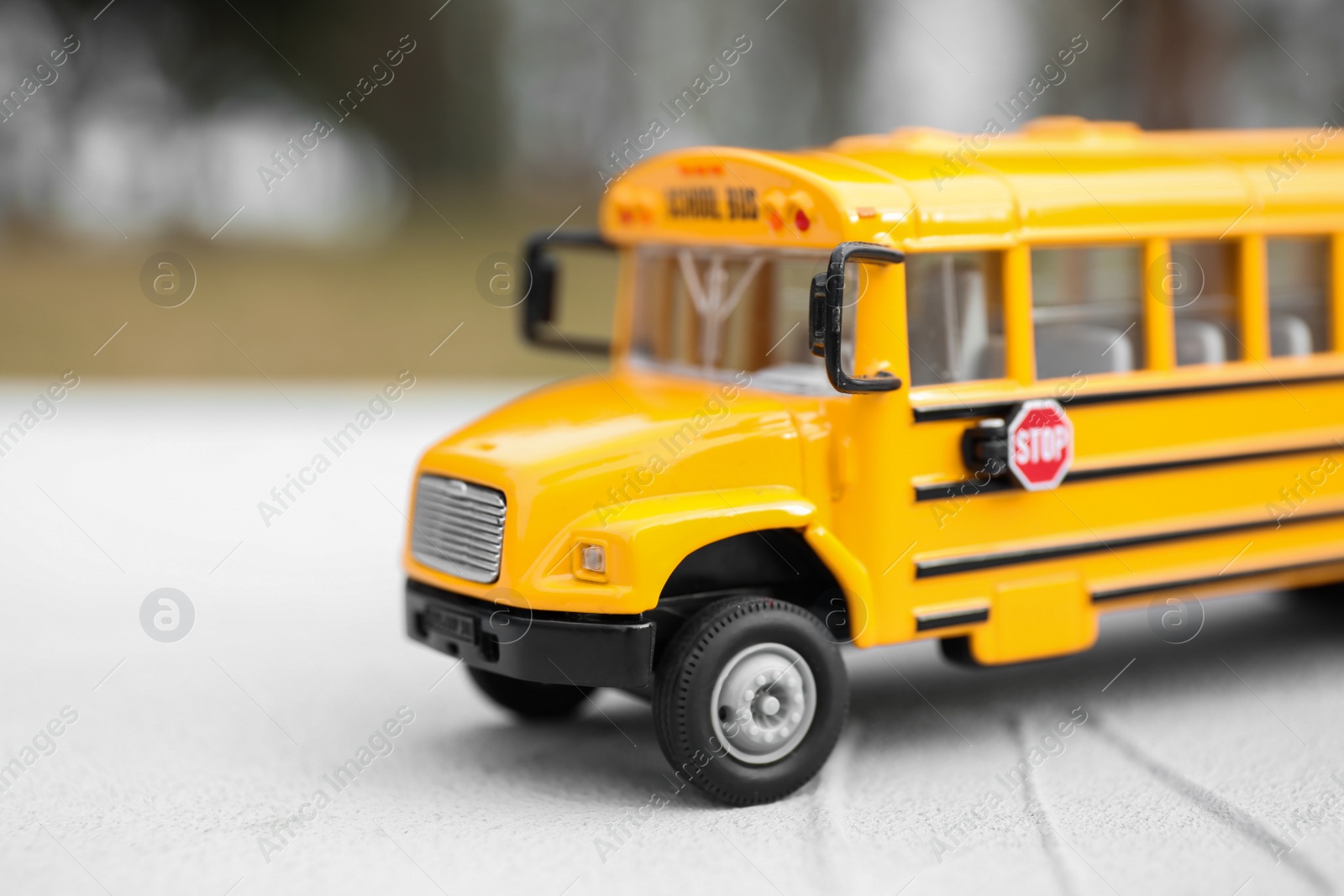 Photo of Yellow toy school bus against blurred 
background, closeup. Transport for students