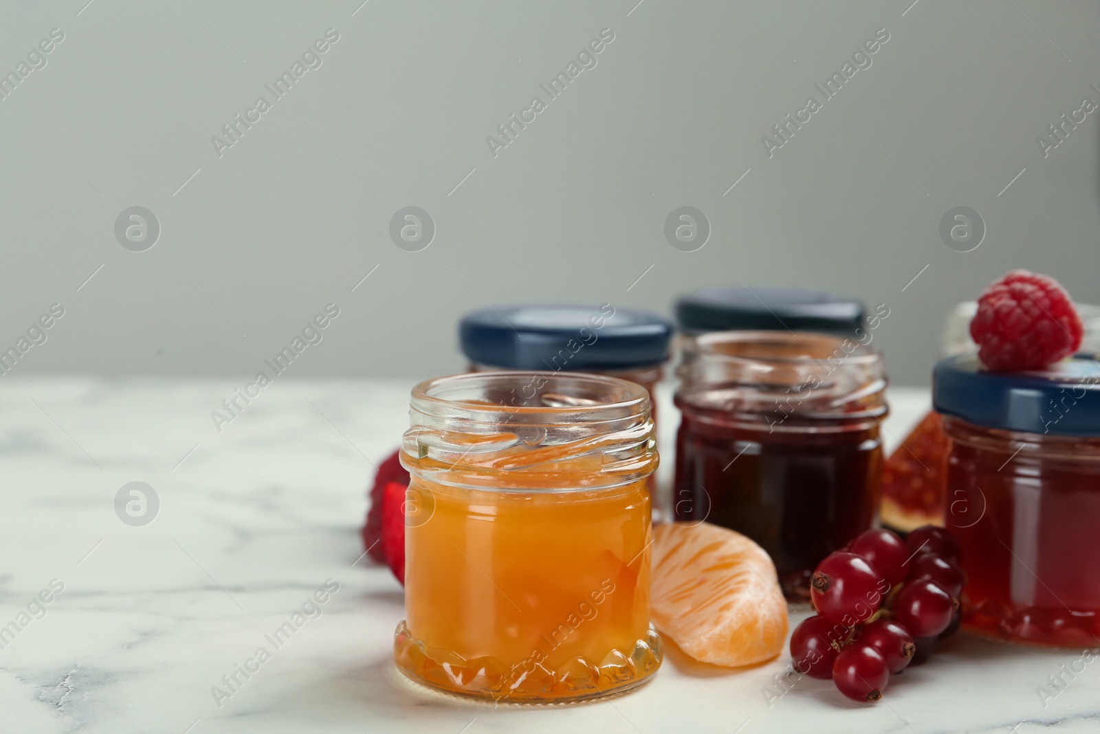 Photo of Jars of different jams and ingredients on white marble table, space for text