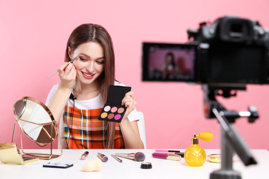 Photo of Beauty blogger filming make up tutorial on pink background