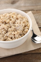 Photo of Tasty boiled oatmeal in bowl and spoon on wooden table, closeup