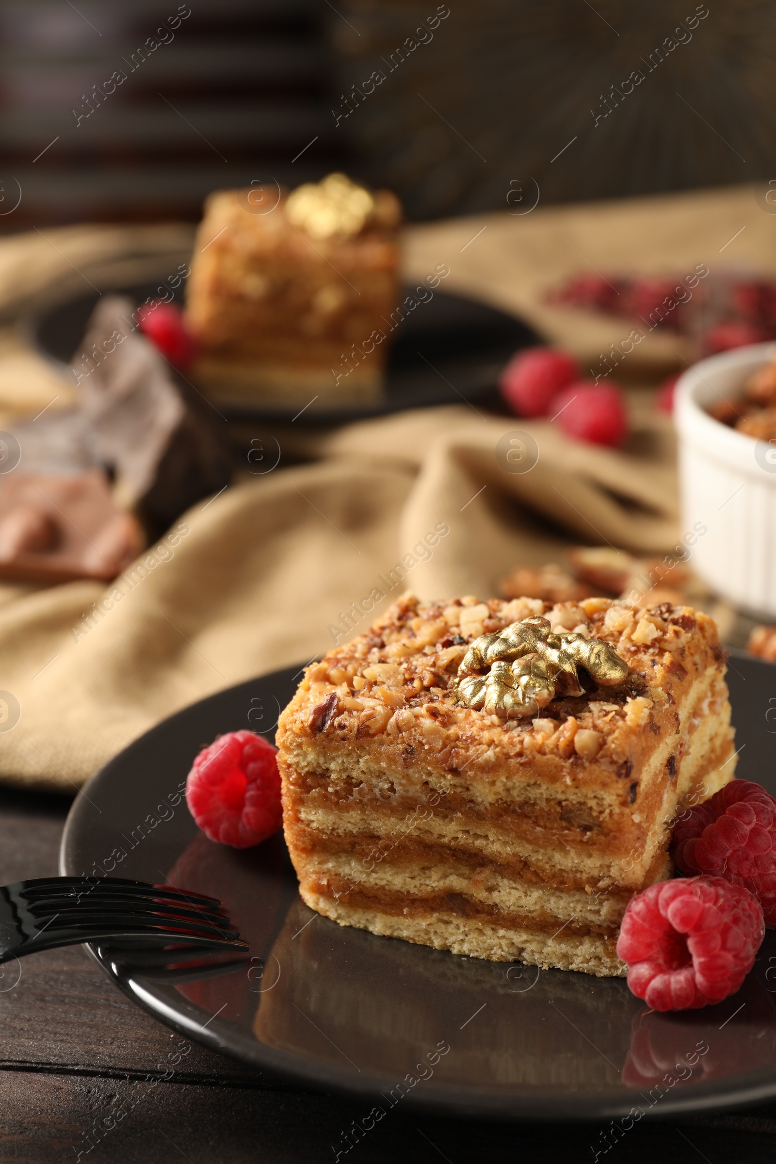 Photo of Pieces of delicious layered honey cake with nuts and raspberries on wooden table, closeup. Space for text