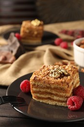 Pieces of delicious layered honey cake with nuts and raspberries on wooden table, closeup. Space for text